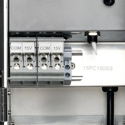 Close-up of an electrical terminal block with four COM and 15V connectors, labeled 15PC150SS, on a metallic panel.