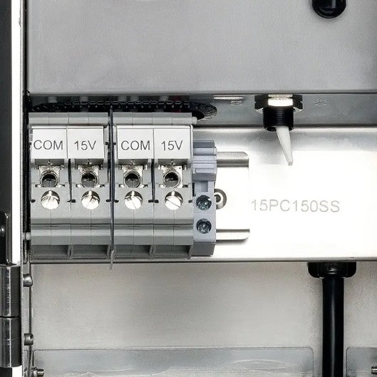 Close-up of an electrical terminal block with four COM and 15V connectors, labeled 15PC150SS, on a metallic panel.