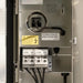 Close-up of an electrical panel door showing a plug-in socket, warning label, terminal connectors labeled COM 15V, and instructional text on a metallic panel.