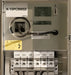 An industrial electrical panel or distribution box labeled K-15PC900SS, with terminal blocks for COM and 15V, warning stickers, and a remote switch handle.