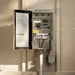 An open Kichler electrical panel mounted on a beige wall, showing the internal terminal blocks, wiring, and switch mechanism. The panel door is open to the left, and the interior metal box is visible against warm sunlight and shadows.
