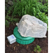 A large natural-looking gray stone or rock placed on top of a round green lid, outdoors in mulch with green plants in the background. A small white control box is also visible beside the setup.