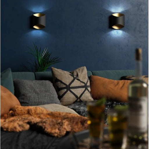 Cozy living room with a blue wall, decorative pillows, and a bottle of wine. and two black wall LED lights with gold trim