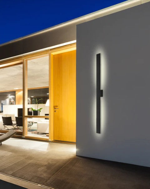 Modern wall-mounted light fixture on a white wall with a living room in the background