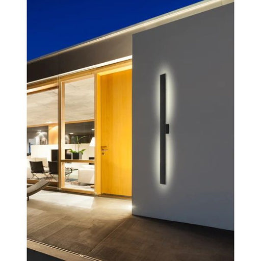 Modern wall-mounted light fixture on a white wall with a living room in the background