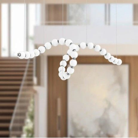 Modern chandelier with white spherical beads in a room with wooden doors and stairs.