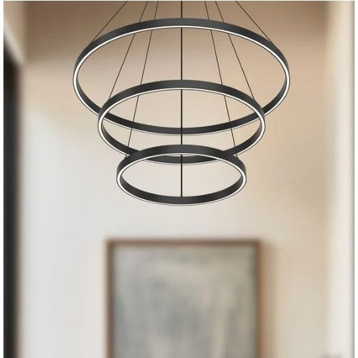 Modern black pendant light with three circular designs hanging against a neutral wall.