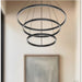 Modern black pendant light with three circular designs hanging against a neutral wall.