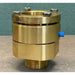 A brass hydraulic or plumbing fitting with a blue side connector, photographed on a neutral surface against a textured green backdrop.